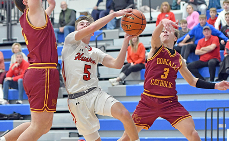 Aurora’s Ryan Staehr splits two Omaha Roncalli defenders on a dribble-drive second half play during a 54-41 loss to the Crimson Pride Monday.