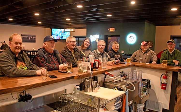 Members of the informal group calling itself “League” sit at the bar of the Loading Chute in Hampton on Monday night. One of the members joked that the group got its name because the men “compete” with the pickleball league that plays at the City Auditorium. With the group is Loading Chute bartender Annette Miller. Members in attendance Monday were, from left: John Kohtz, Tom Williamsen, Gene Winter, Tom Lindburg, Ed Dick, Robin Williamsen and Dean Klute.
