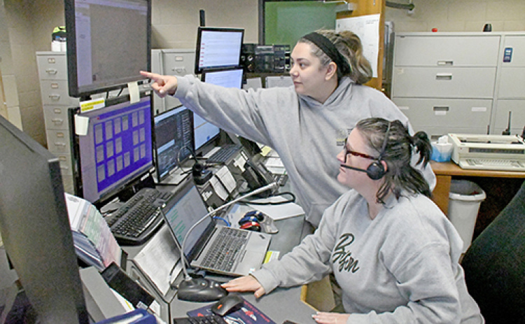 Headsets allow 911 dispatchers at the Hamilton County Dispatch Center to have their hands free while they are taking calls from the public. The tabletop microphone in front of dispatcher Jessie Boroff (seated) is used for contacting police officers and other personnel in the field. Also pictured is fellow dispatcher Melissa Barry.
