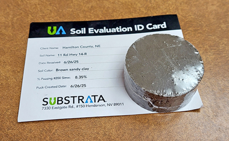 County Highway Supt. Jeremy Brandt sent a sample of the material dug from about six inches below the surface of 11 Road to Substrata, the Nevada company that manufactures Perma-zyme, and received back this shrink-wrapped puck made from the sample by adding the ezyme to it. It appears to be as hard as concrete.