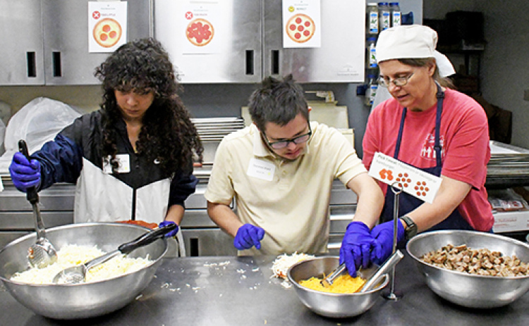 A student takes his turn at dressing one of the 130 personal pan pizzas that were served for lunch at The Leadership Center’s VLS Summit held on Thursday for 75 special needs students from across Nebraska.