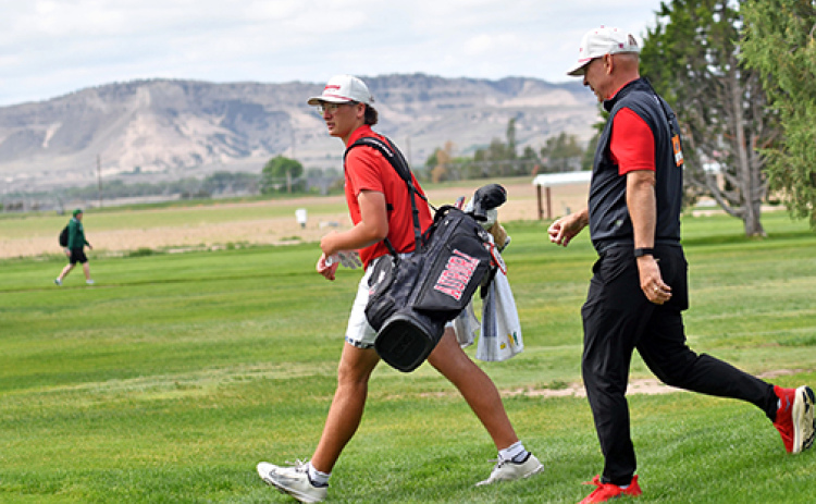 Cash Garrett walks off the No. 11 tee box at Scottsbluff Country Club with the Bluffs in the background and coach Craig Badura in tow.