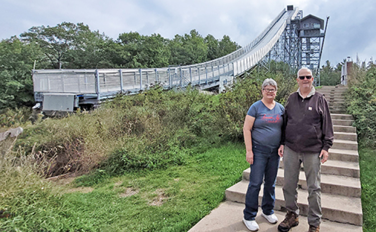 Tom and Patti Kell stand next to the imposing Pine Mountain Ski Jump in Michigan, which at 176 feet is one of the highest artificial ski jumps in the world. “Scary to even be on the ground imagining the jump,” Patti observed.  The jump is located across the river from the small town of Aurora, Wisc.