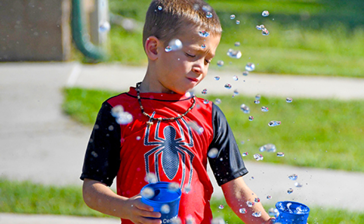 Luke Janzen fills up cups with water from the splash pad’s fountains during his family’s visit in the Thursday afternoon heat. The splash pad in Cole Park is now closed for the season.