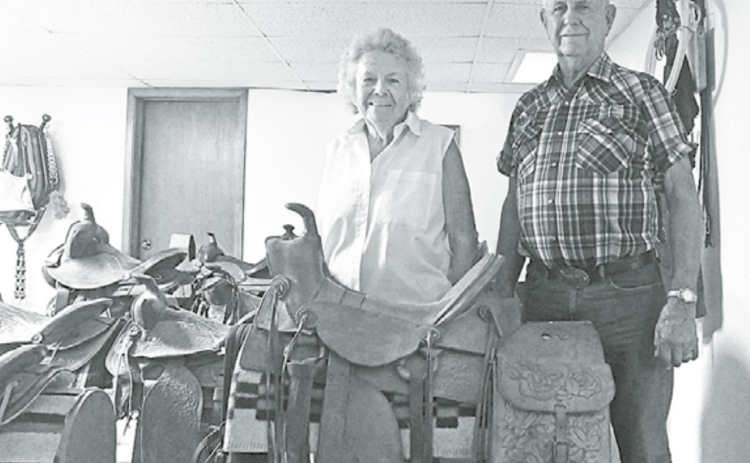 Elvera and Dwight Willcock stand with his favorite saddle among his collection. This saddle was a gift from his uncle and was used until they sold their last working horse. News-Register/Jeni Moellenberndt