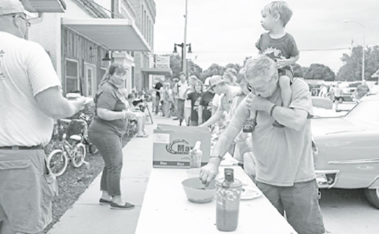 Hampton Public Schools staff members Joel Miller (left) and Jan Ediger help to pass out free BBQ pulled pork meals to the public, courtesy of the Roger Bamesberger family. The line stretched down the block. News-Register/Cheyenne Rowe