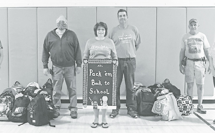 Marilyn Vrana (left), David Olson, Holly Schmit, Phil Troester, Bob Spotanski and Laura Jobman stand with a portion of the 93 donated backpacks for students at Aurora Elementary and Middle School. News-Register/Jeni Moellenberndt